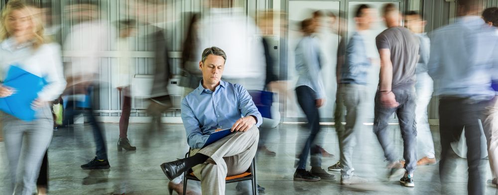 A white man sits in a chair while people around him are blurred